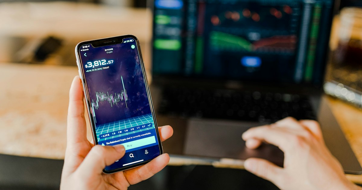 Смартфон с графиком котировок в руке, на фоне ноутбук с торговым терминалом